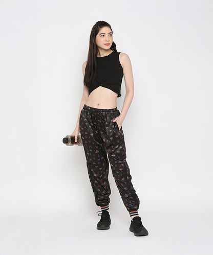 A woman poses against a white background wearing a Black Twisted Crop Top, printed joggers, and sneakers while holding a water bottle.