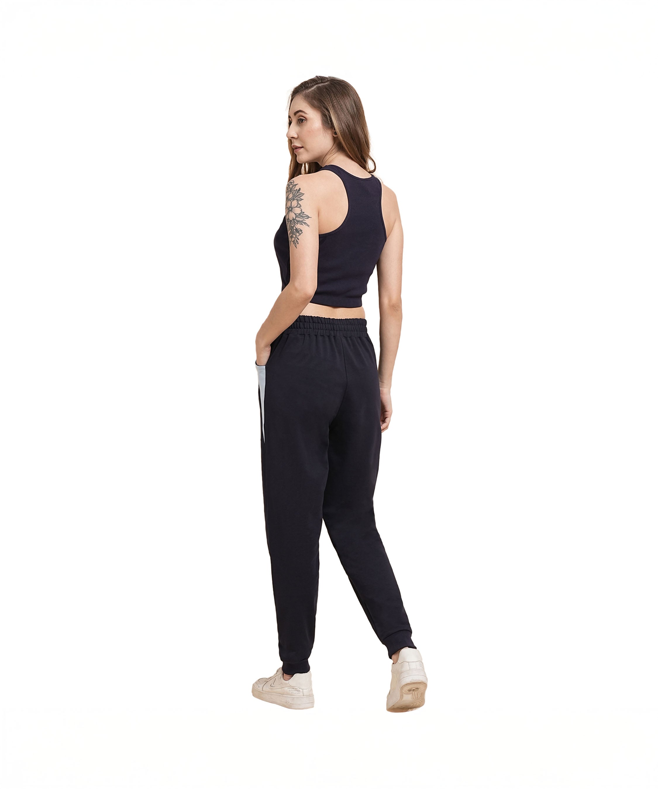 Woman in a navy blue ribbed crop top and joggers stands on a white background, looking over her shoulder.