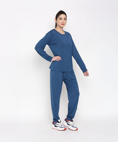 A woman models the Atlantic Blue Active Duo—cotton modal joggers paired with a blue racerback top—and white sneakers, standing against a plain white background.