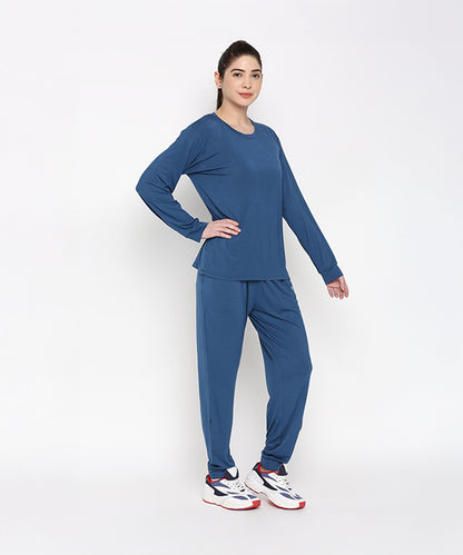 A woman models the Atlantic Blue Active Duo—cotton modal joggers paired with a blue racerback top—and white sneakers, standing against a plain white background.
