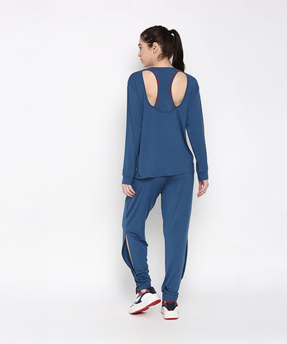 Woman in Atlantic Blue Active Duo—blue racerback top crafted from buttery soft fabric and cotton modal joggers—sporting a ponytail and white sneakers, facing away.