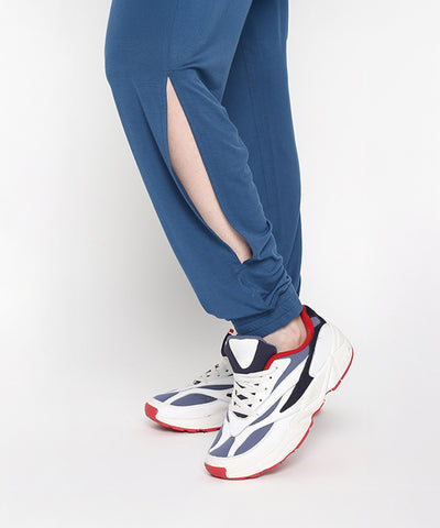 Wearing the Atlantic Blue Active Duo pants, known for their buttery soft fabric and side slit, styled with white sneakers featuring navy and red accents while standing on tiptoe.
