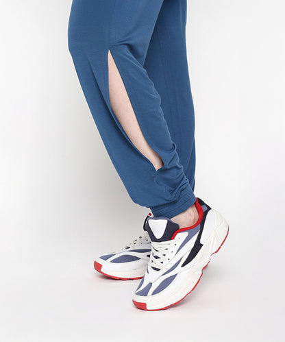 Wearing the Atlantic Blue Active Duo pants, known for their buttery soft fabric and side slit, styled with white sneakers featuring navy and red accents while standing on tiptoe.
