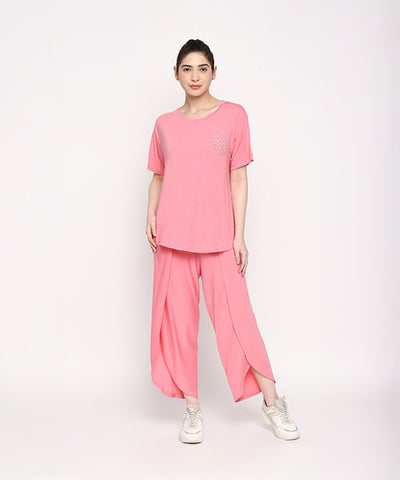 A woman stands against a plain white background wearing the Coral Blissful Tulip Set, featuring a coral pink Cotton Modal top and matching tulip pants.