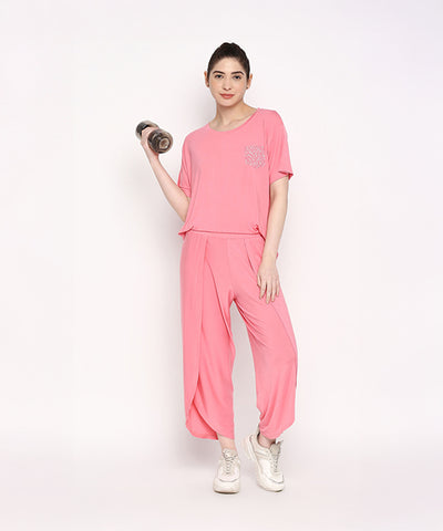 Woman wearing the Coral Blissful Tulip Set, made from Cotton Modal, balances on one leg and holds a dumbbell against a plain white background.