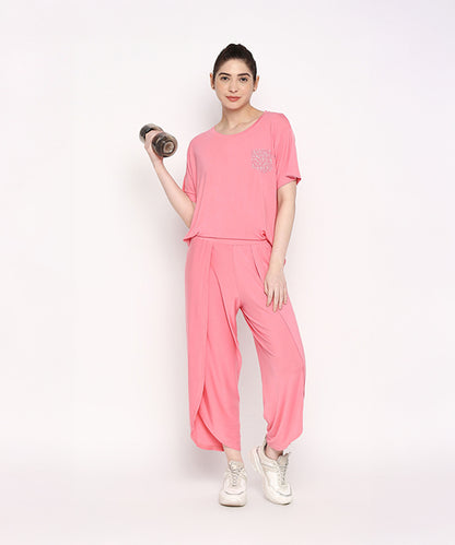 Woman wearing the Coral Blissful Tulip Set, made from Cotton Modal, balances on one leg and holds a dumbbell against a plain white background.
