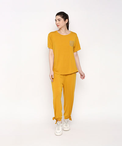 A woman wears the Mustard Chic Set—mustard yellow top and cotton modal trackpant pajama with soft elasticated waistband—paired with white sneakers, standing against a plain white background.