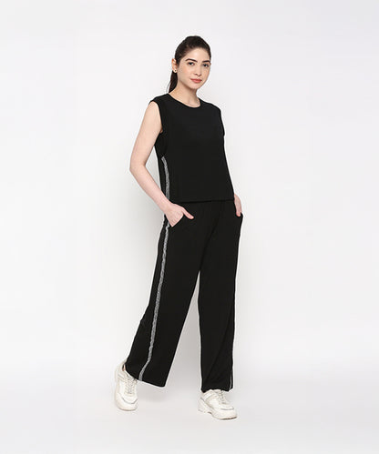 Woman wearing the Comfy Black Set with Side Sparkle—sleeveless top and loose fit track pants with side stripes—posing with hands in pockets.