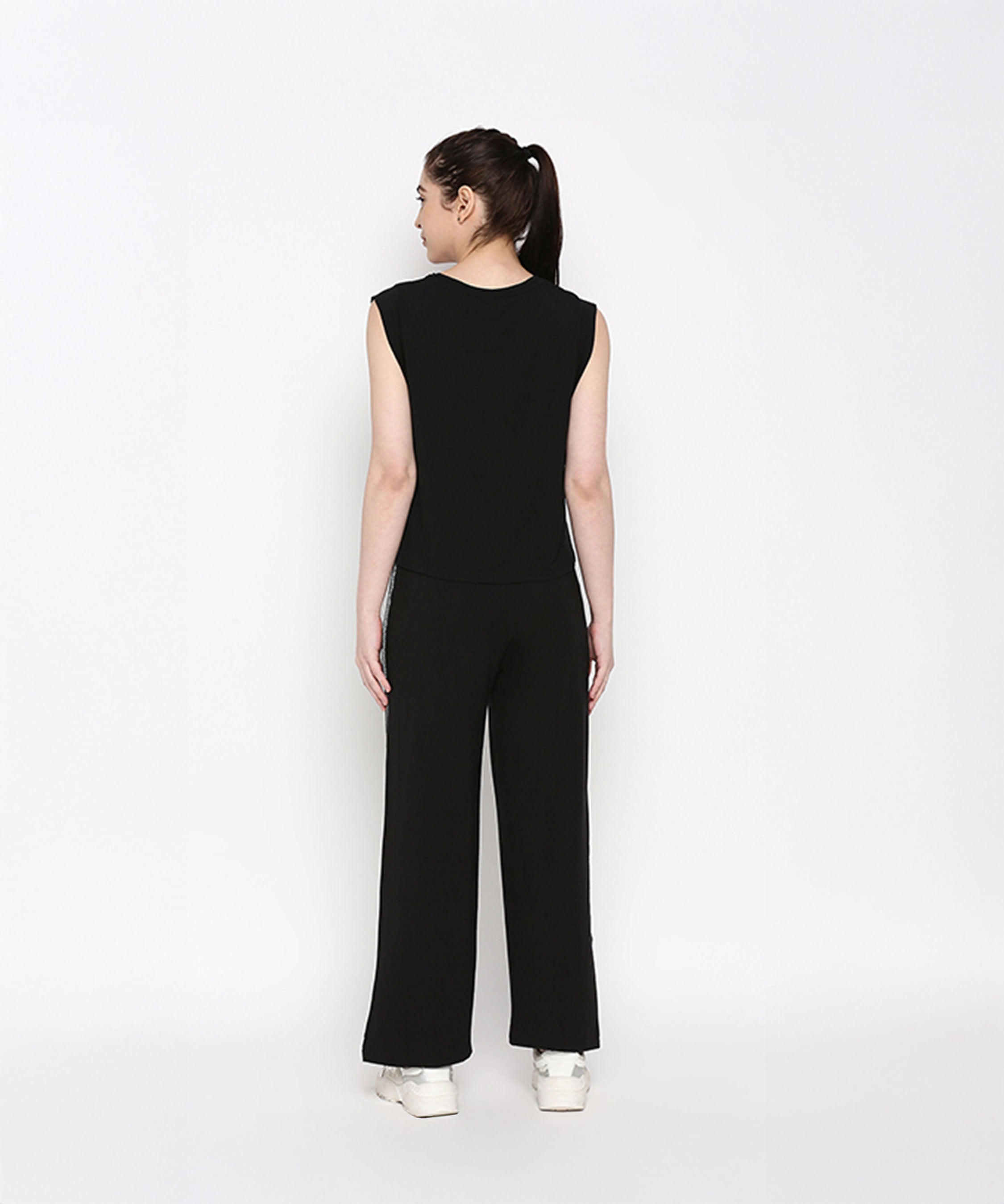 Woman wears the Comfy Black Set with Side Sparkle—black sleeveless top and loose-fit track pants with a glitter patch—standing with her back to the camera against a white background.