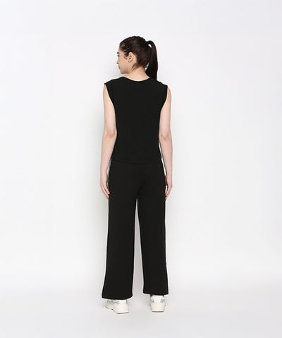 Woman wears the Comfy Black Set with Side Sparkle—black sleeveless top and loose-fit track pants with a glitter patch—standing with her back to the camera against a white background.