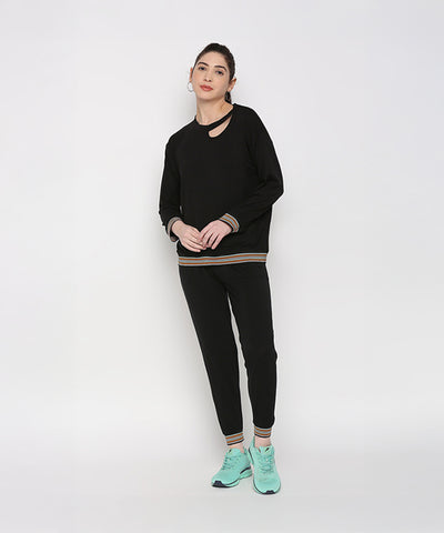 Model wears the Versatile Black Ensemble—black joggers and a black neck cut out top—paired with teal sneakers, standing against a plain white background.