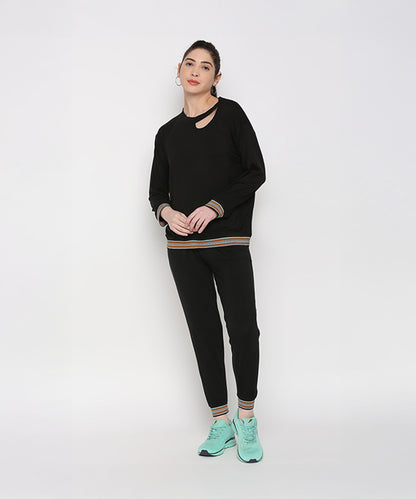 Model wears the Versatile Black Ensemble—black joggers and a black neck cut out top—paired with teal sneakers, standing against a plain white background.