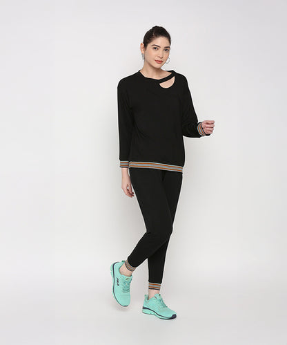 Woman showcasing the Versatile Black Ensemble featuring a black neck cut out top and cotton modal joggers, paired with teal sneakers, against a plain white background.