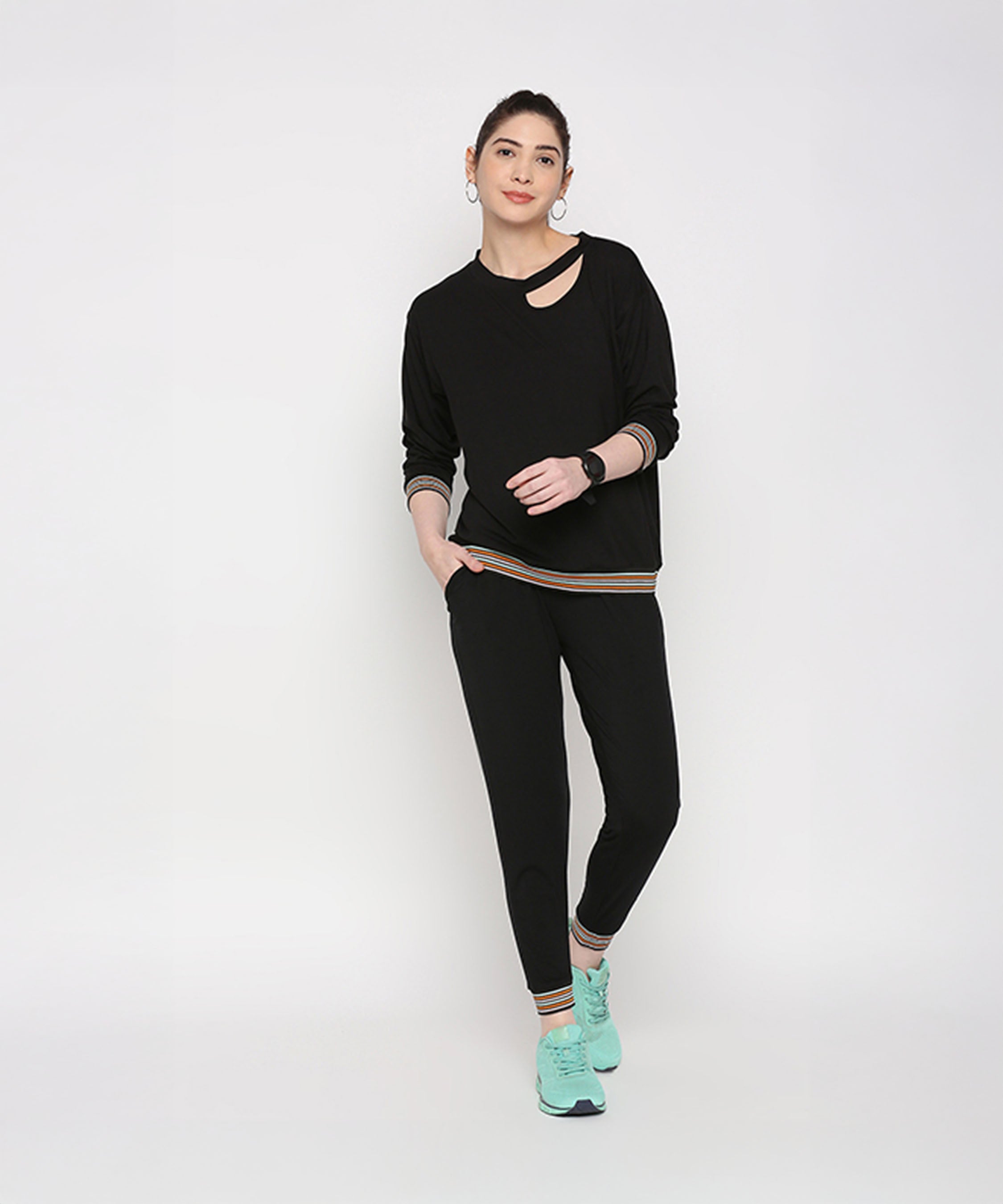 Woman models the Versatile Black Ensemble, featuring cotton modal joggers and turquoise sneakers, against a plain white background.