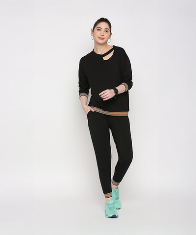 Woman models the Versatile Black Ensemble, featuring cotton modal joggers and turquoise sneakers, against a plain white background.