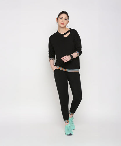 Woman models the Versatile Black Ensemble, featuring cotton modal joggers and turquoise sneakers, against a plain white background.