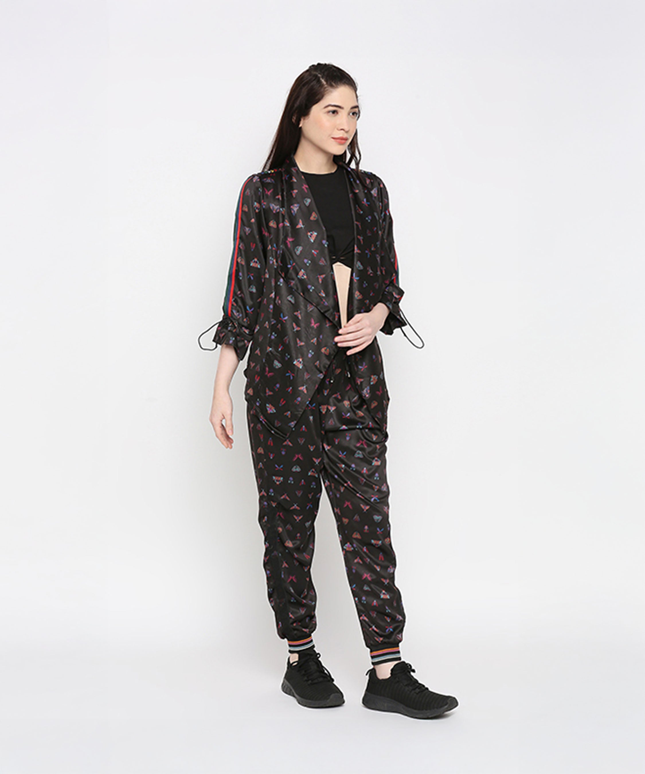 A woman stands against a plain white background wearing Tuna Active Butterfly Joggers with black sneakers, styled as part of a black co-ord set.