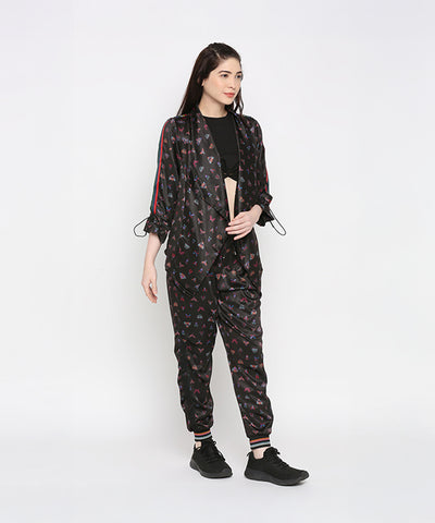 A woman stands against a plain white background wearing Tuna Active Butterfly Joggers with black sneakers, styled as part of a black co-ord set.
