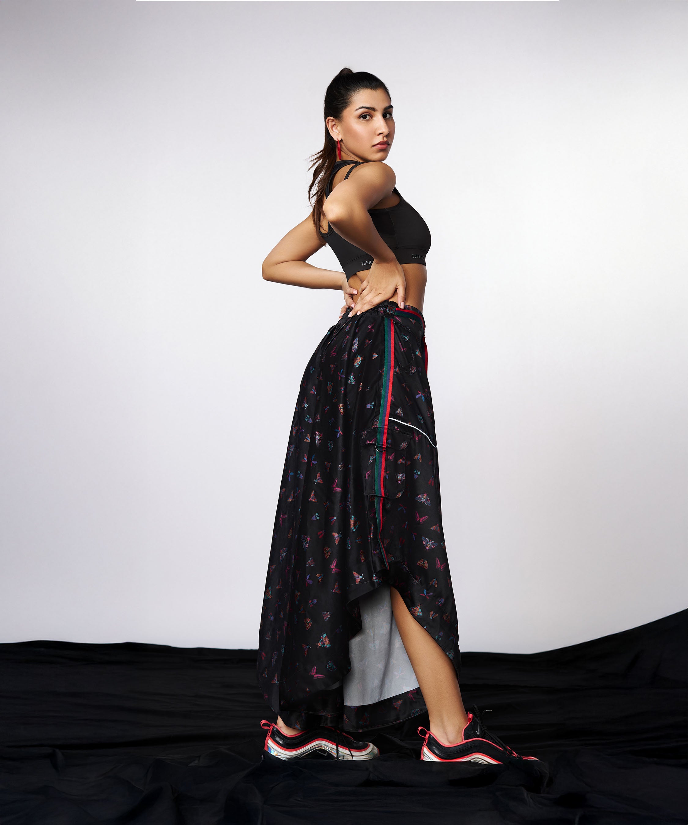 A woman confidently poses in the Tuna Active Co-ord Set—yoga pants and jacket—featuring a sporty black look with butterfly prints, paired with sneakers against a plain background.