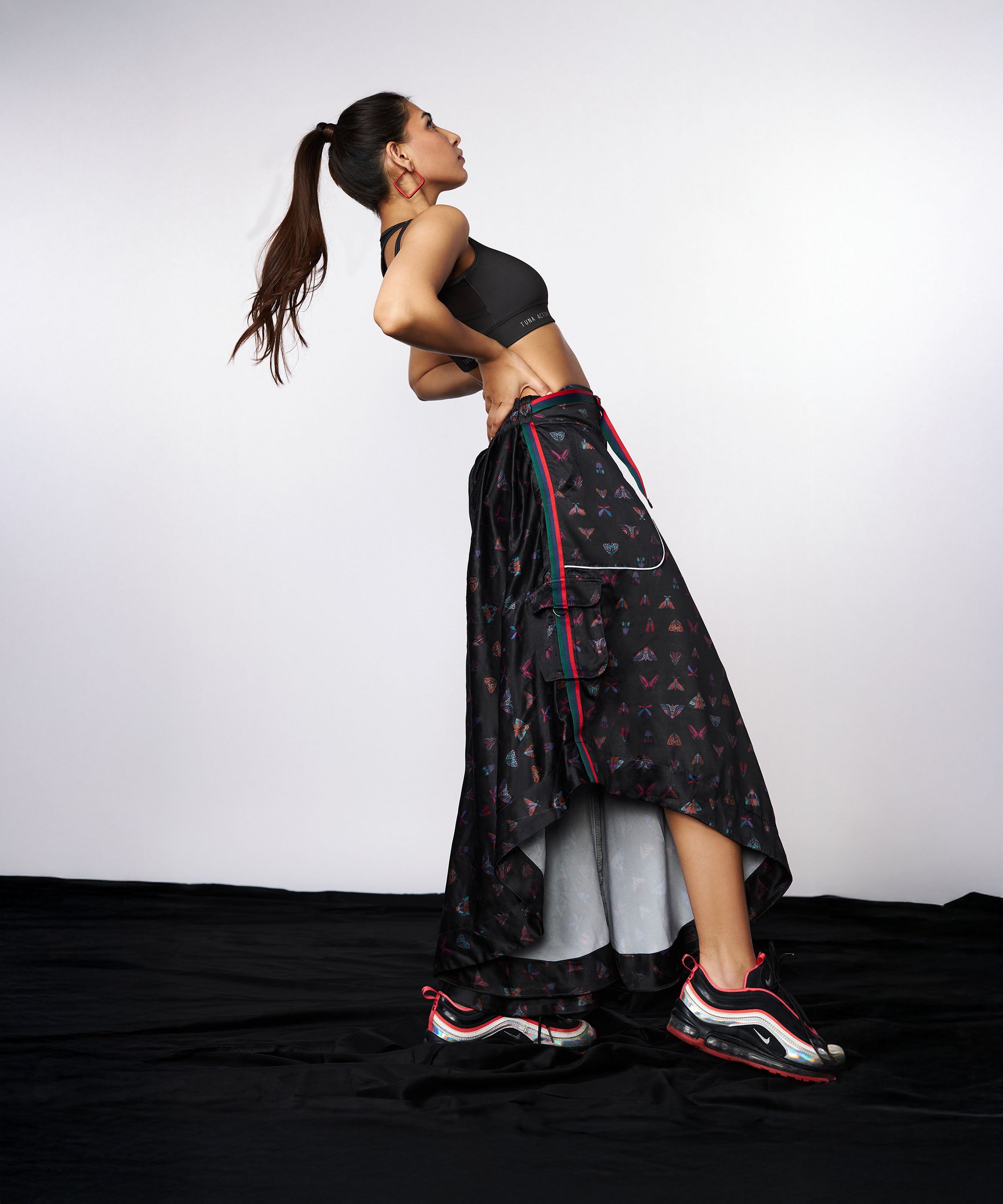 A woman in a sporty pose, hands on her lower back, wears the Tuna Active Co-ord Set—yoga pants featuring a butterfly print and cargo pocket, paired with a matching black crop top and jacket.