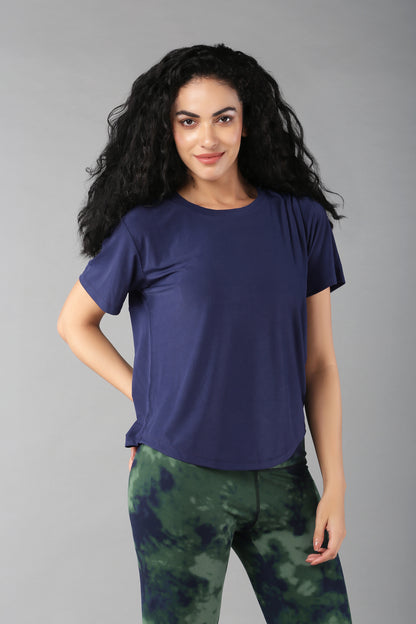 Woman with curly hair wearing the Functional - Blue Soft T Shirt and green tie-dye leggings, standing against a gray background—a versatile outfit for stylish adventures.