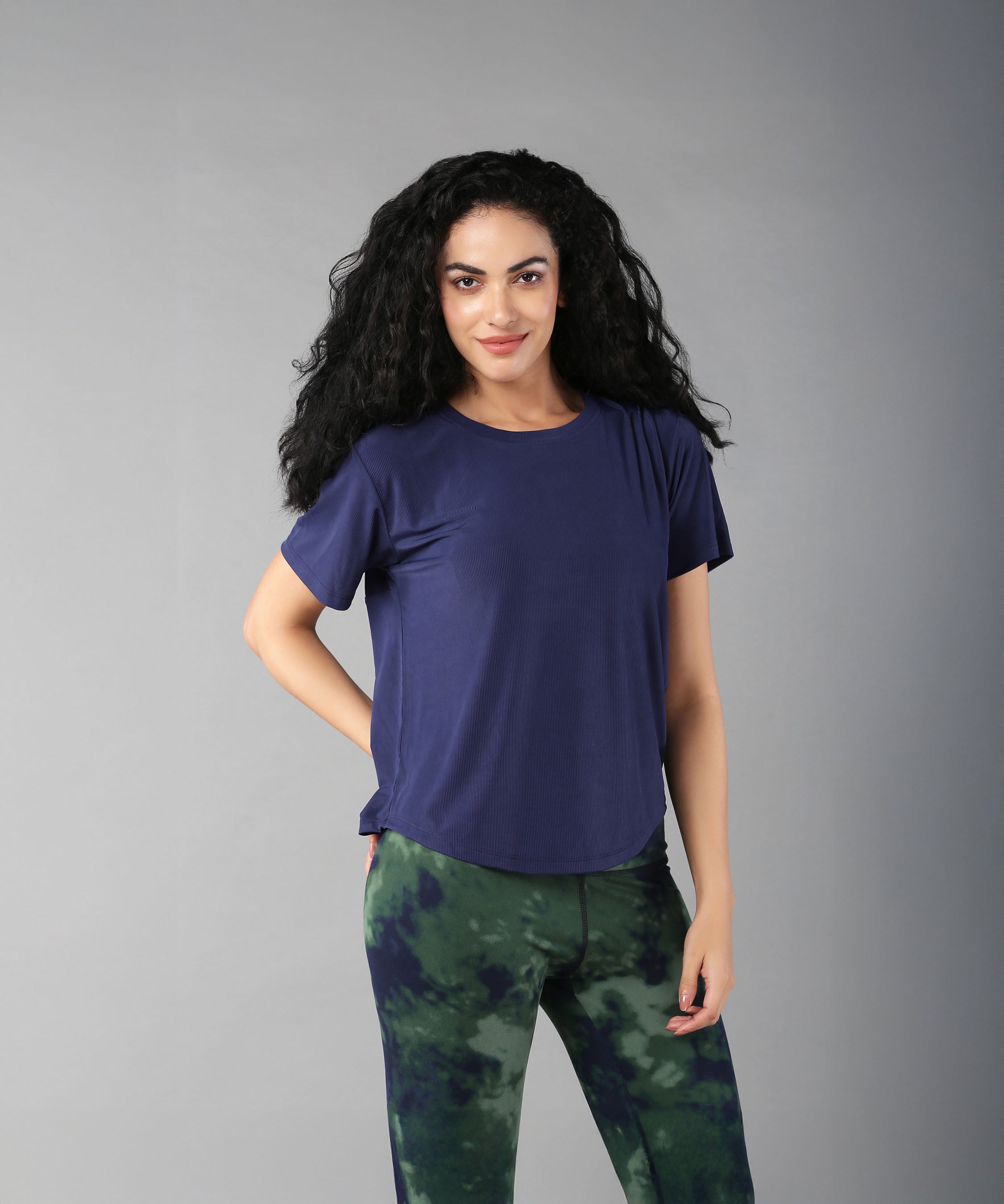 A woman with long curly hair wears the Functional - Blue Soft T Shirt, made from durable, comfortable materials, standing against a plain gray background.