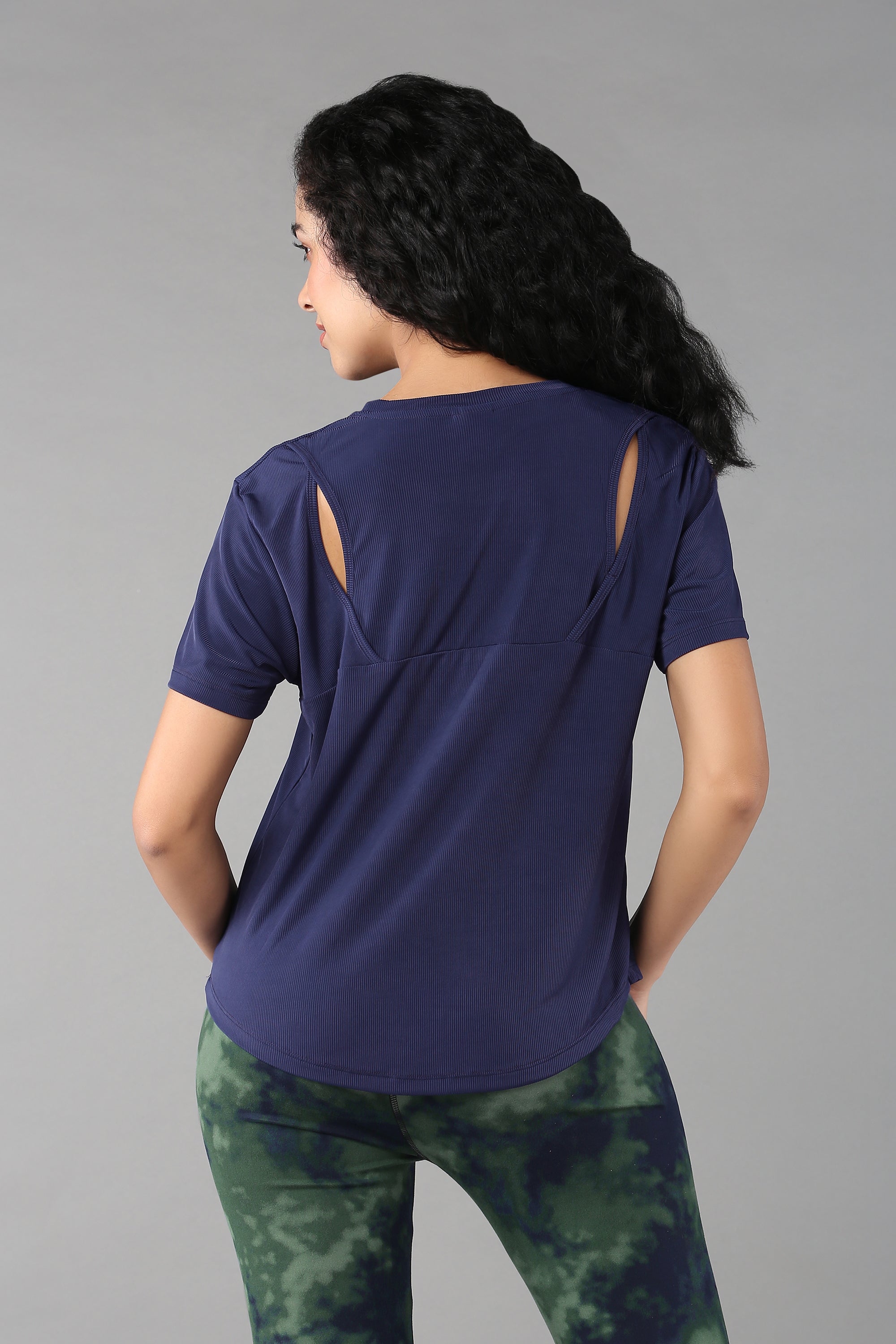 A woman with long dark hair wears the Functional - Blue Soft T Shirt and green tie-dye leggings—a stylish, versatile outfit for exploring the world.