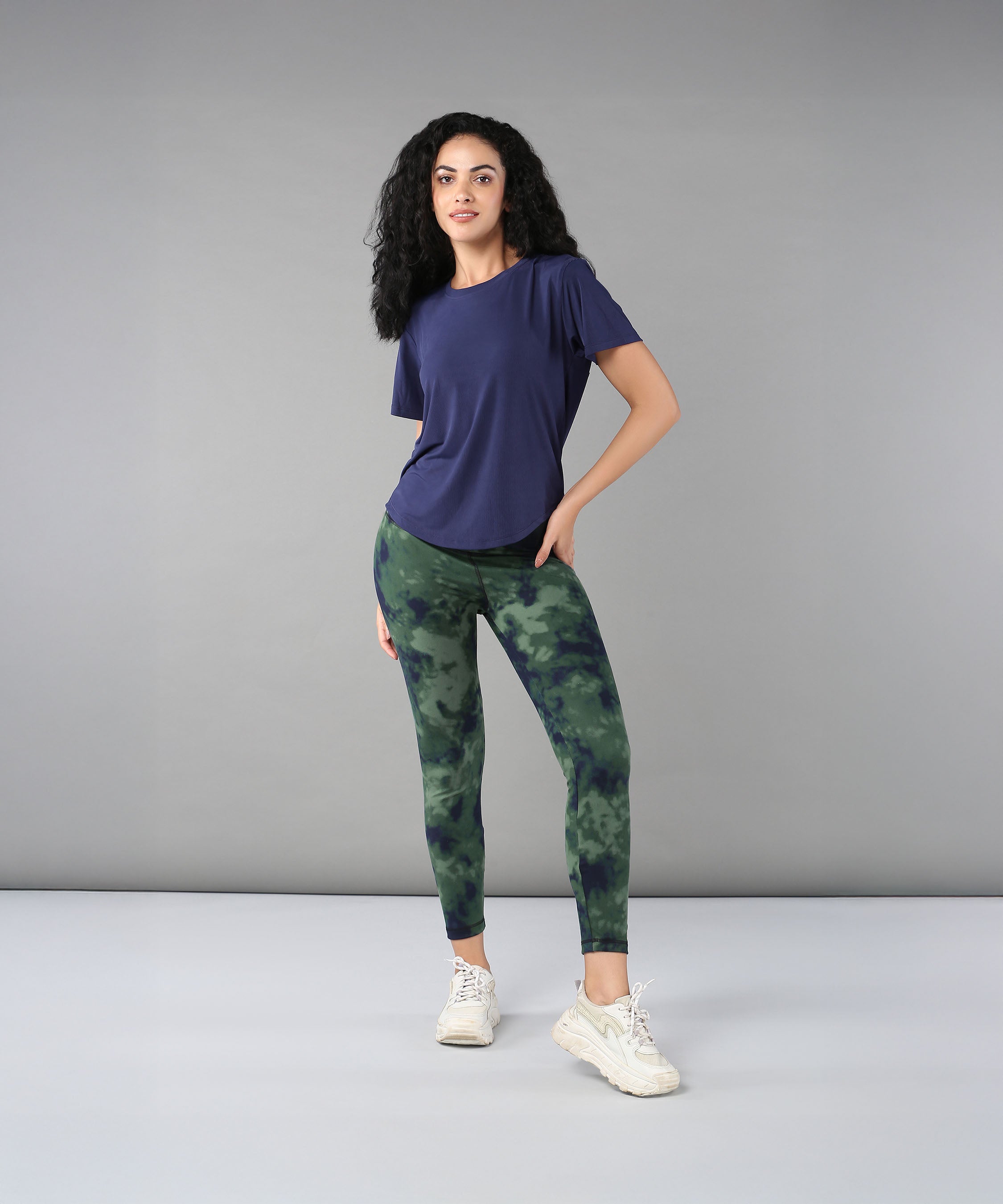 Woman in a blue Functional Soft T Shirt stands against a plain gray background, showcasing a poly blended top perfect for versatile outdoor clothing needs.