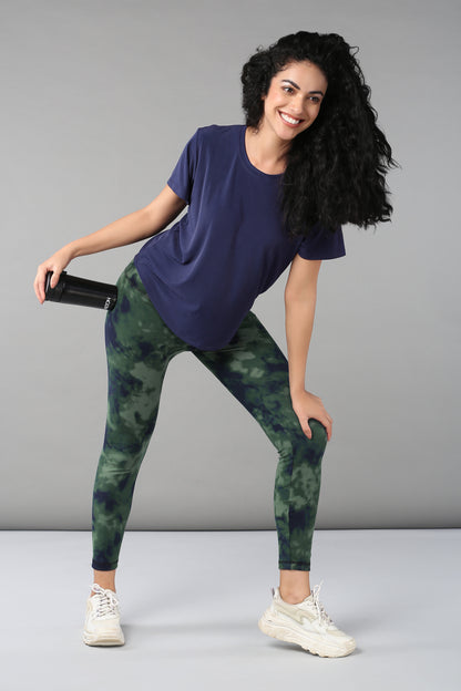 Woman in the Functional - Blue Soft T Shirt, smiling and holding a water bottle, stands relaxed against a plain background—ready to explore the world in style with this versatile top.