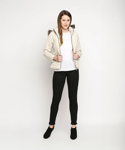 A woman wearing an Off White Mid Length High Collar Puffer Jacket With Detachable Fur Hoodie, a white shirt, black pants, and black shoes stands against a white background.