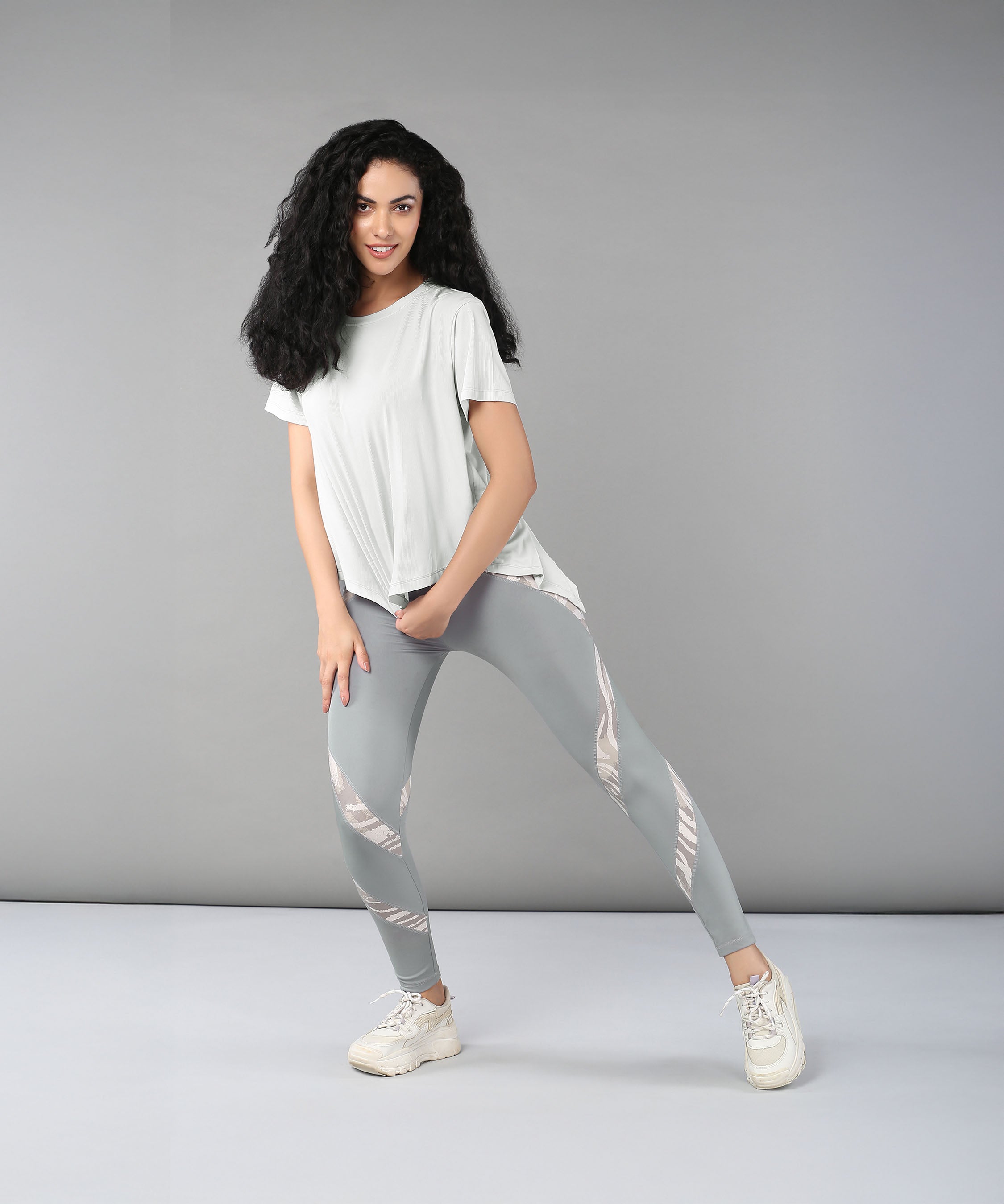 A woman poses confidently against a plain gray background wearing the Grey Top with Patched Legging, showcasing light, moisture-wicking fabric and bold patterns.