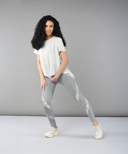 A woman poses confidently against a plain gray background wearing the Grey Top with Patched Legging, showcasing light, moisture-wicking fabric and bold patterns.