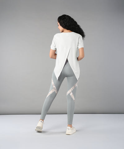 Woman with long curly hair, wearing the Grey Top with Patched Legging made from super soft fabric, stands facing away in a studio.