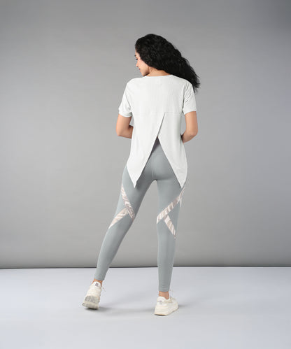 Woman with long curly hair, wearing the Grey Top with Patched Legging made from super soft fabric, stands facing away in a studio.