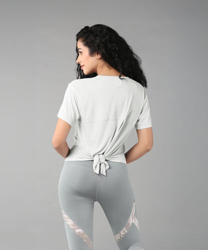 Woman in grey top with patched legging, featuring a knotted back t-shirt made from super soft fabric and patterned leggings, on a plain background.