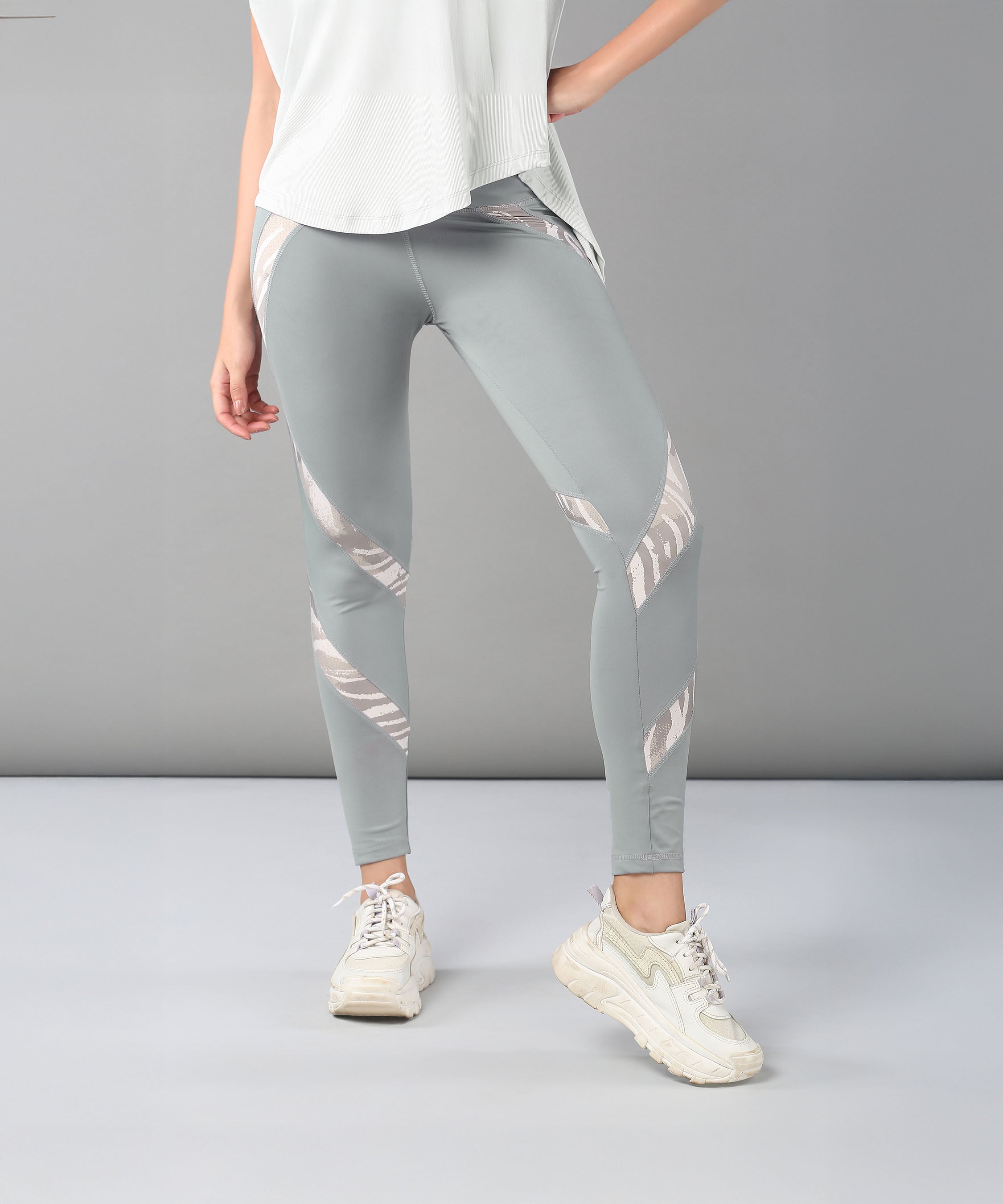 Model wears the Grey Top with Patched Legging, featuring light gray leggings with shiny silver stripes, paired with a white top and white sneakers against a plain background.