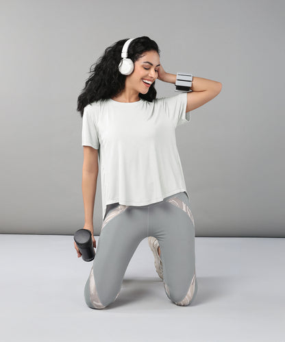 Smiling woman kneeling with headphones and holding a water bottle, dressed in the Grey Top with Patched Legging—workout clothes made from super soft fabric for all-day comfort.