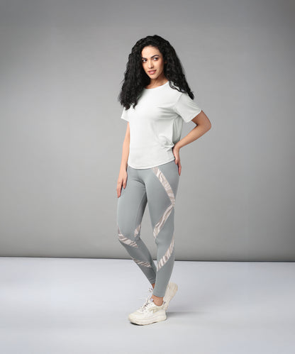 A woman showcases the Grey Top with Patched Legging, posing in a studio with a neutral gray background to highlight its super soft fabric and modern cross body design.