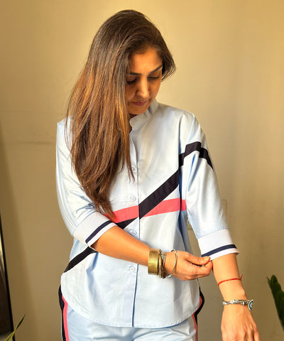A woman in a Contrast Cross Batwing Shirt With Wide Legged Bottom, made of light blue 100% cotton, rolls up her batwing sleeve and looks down, showing bracelets and a red thread on her wrist.