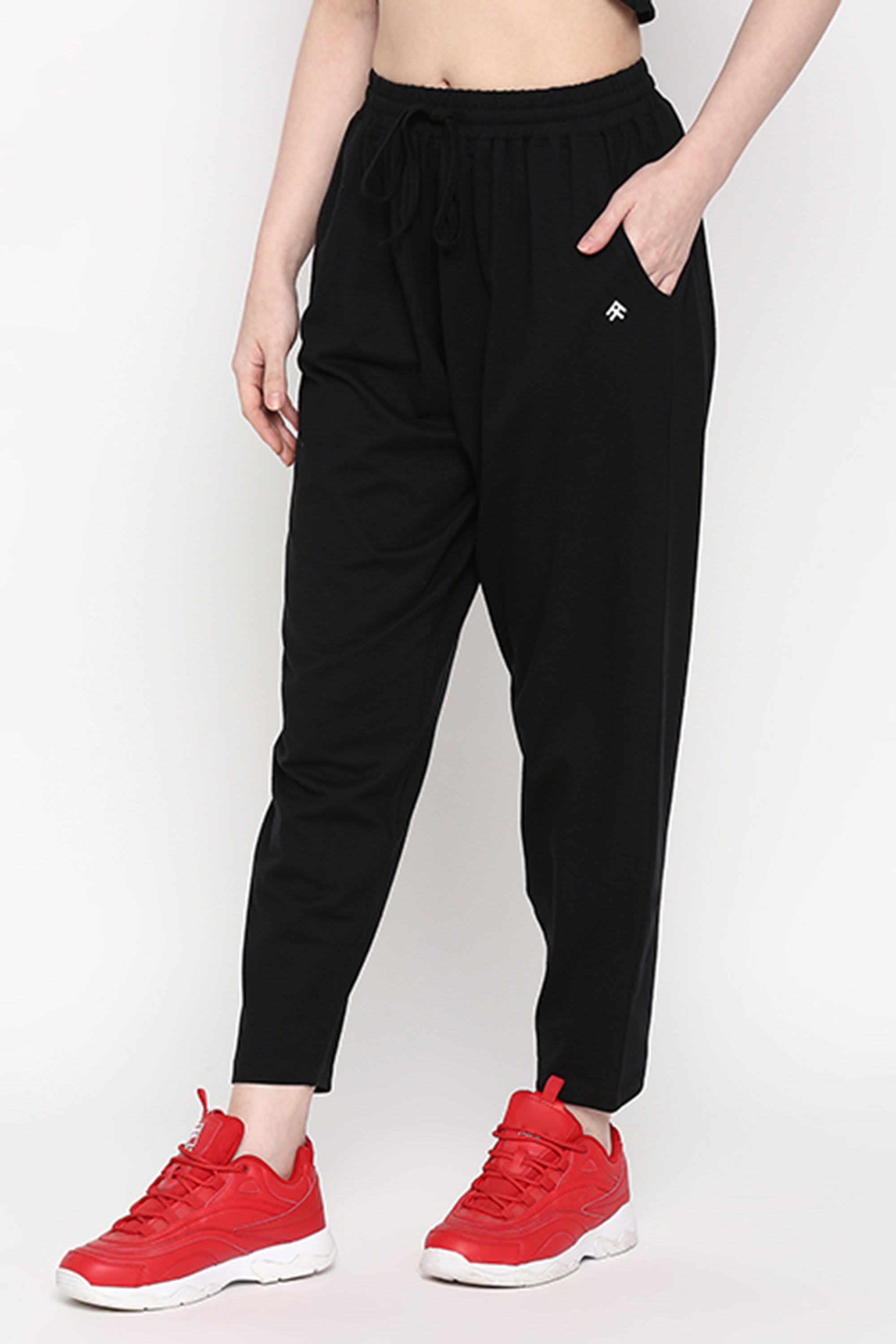 A person wears stretchable black Yoga Pants with hands in pockets and red sneakers, standing against a plain white background.