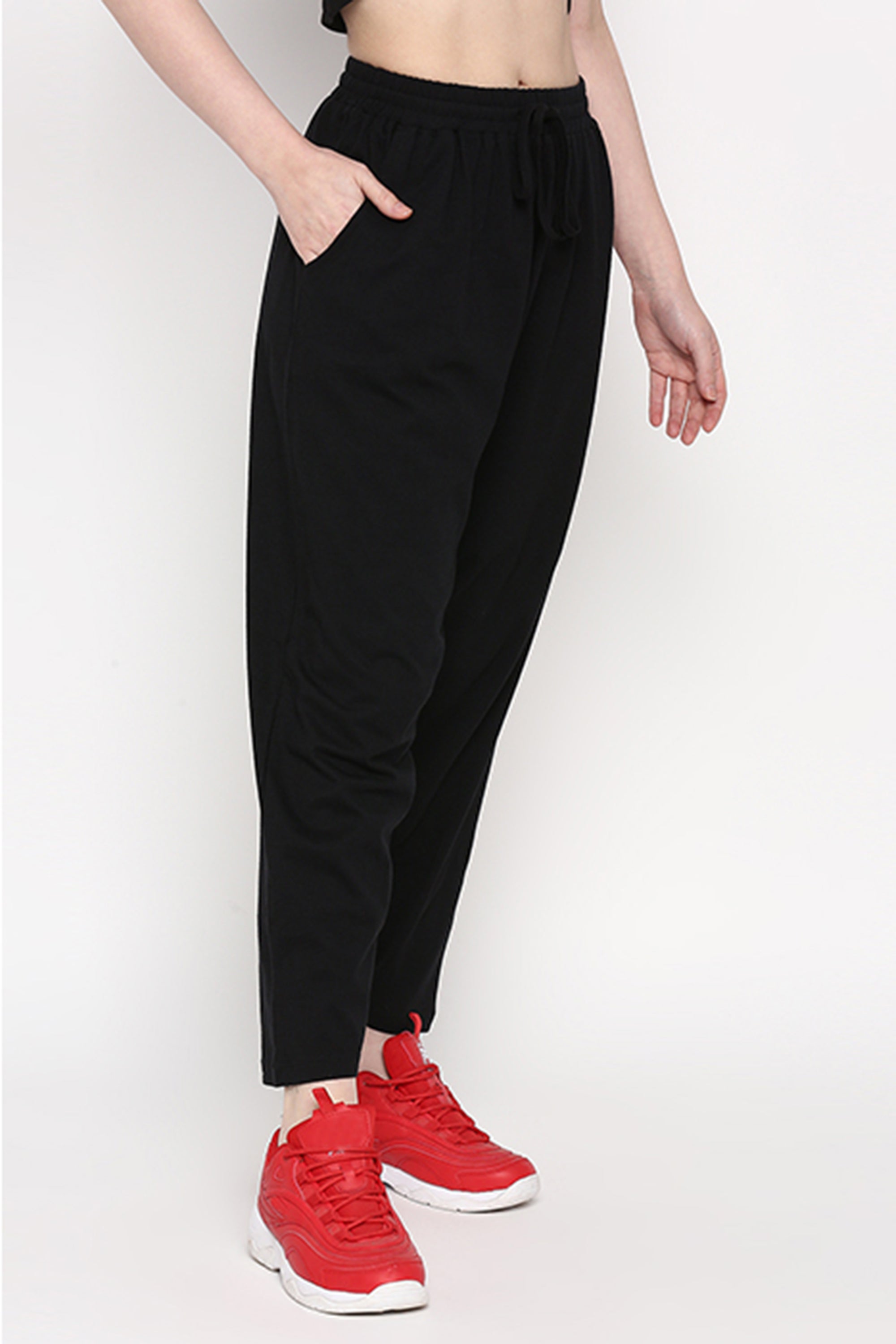 Person wearing black Yoga Pants with hands in pockets and red sneakers, standing against a white background.