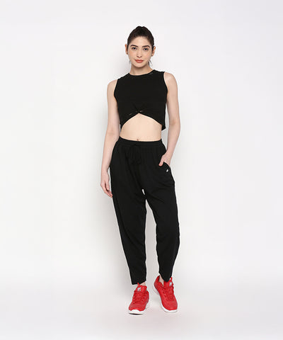 Woman wearing relaxed fit Yoga Pants and a black sleeveless crop top with red sneakers, standing against a plain white background.
