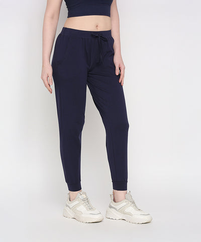 A woman stands against a white background wearing Blue Classic Joggers TLC04 with a slim tapered fit, paired with white sneakers and a black crop top.