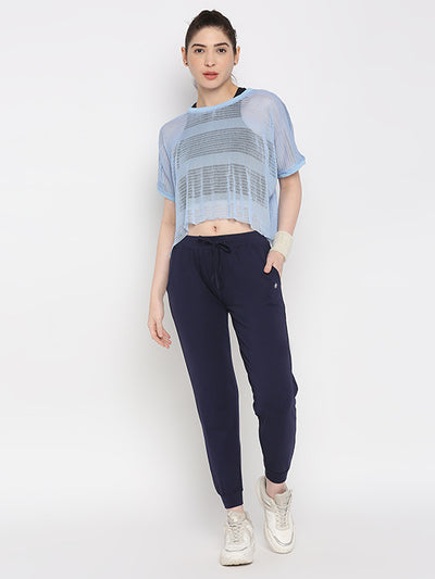 Woman in a light blue sheer top, Blue Classic Joggers TLC04 with a slim tapered fit, and white sneakers posing against a plain white background.