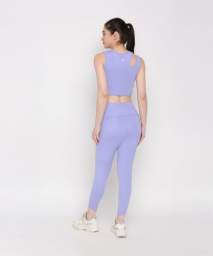 Woman wearing the Tuna Active Lavender Co-ord Set—lavender crop top and leggings—stands in white sneakers against a plain white background, facing away.