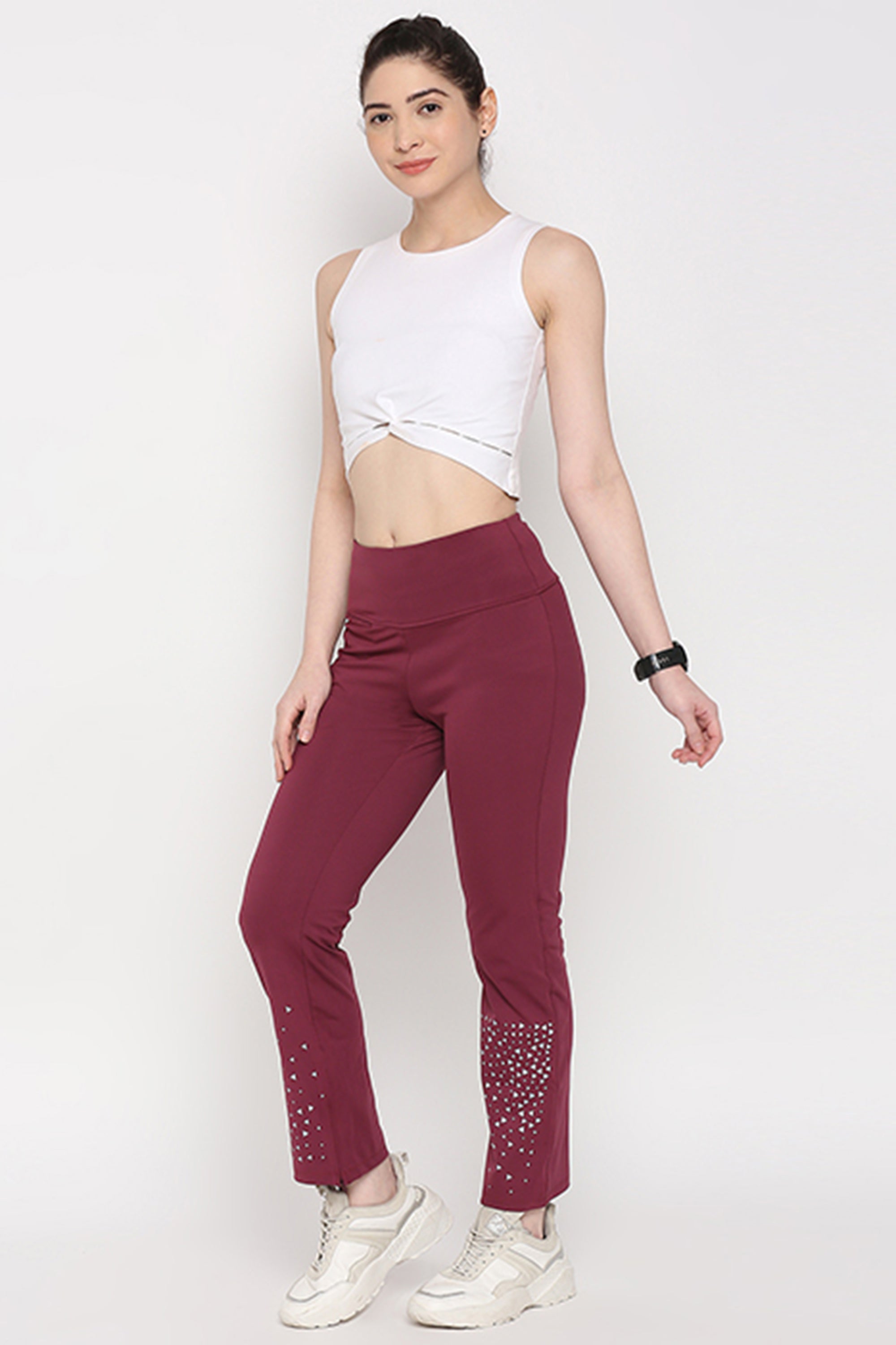 A woman wearing a White Twisted Crop Top with maroon pants and white sneakers stands against a plain background.