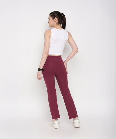A woman faces away from the camera on a white background, wearing Tuna Active Wine Color Boot Cut Pants paired with a white sleeveless crop top.