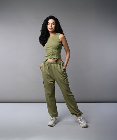 A woman with long dark hair models the Olive Corset Crop - Top with Parachute Pants, standing hands-in-pockets against a gray background.