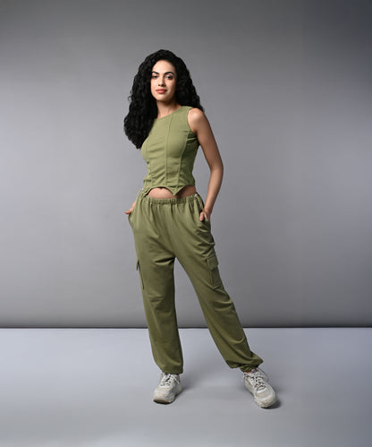 A woman with long dark hair models the Olive Corset Crop - Top with Parachute Pants, standing hands-in-pockets against a gray background.