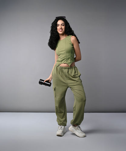 Woman wearing the Olive Corset Crop - Top with Parachute Pants, holding a water bottle and smiling against a plain grey background.